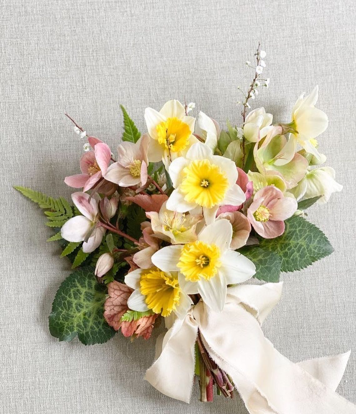 Bouquet of yellow daffodils and pink hellebores tied with a cream ribbon.