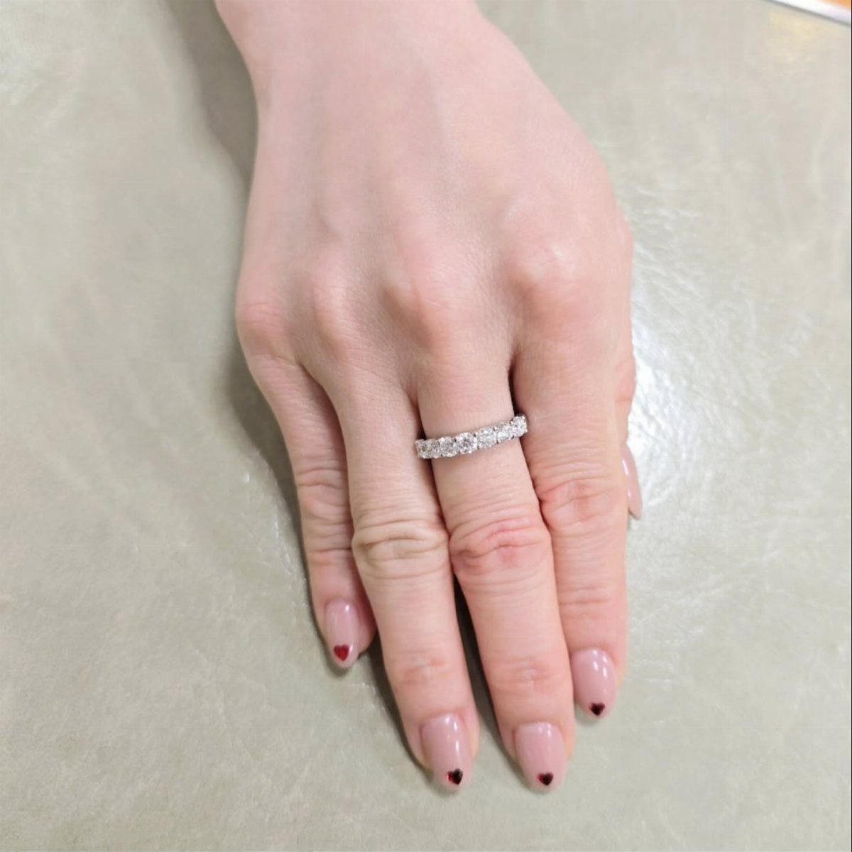 Diamond ring on a finger with pink nails and small red heart tips.