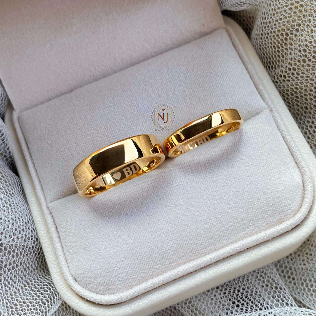 Two gold wedding rings with engravings inside a white jewelry gift box.