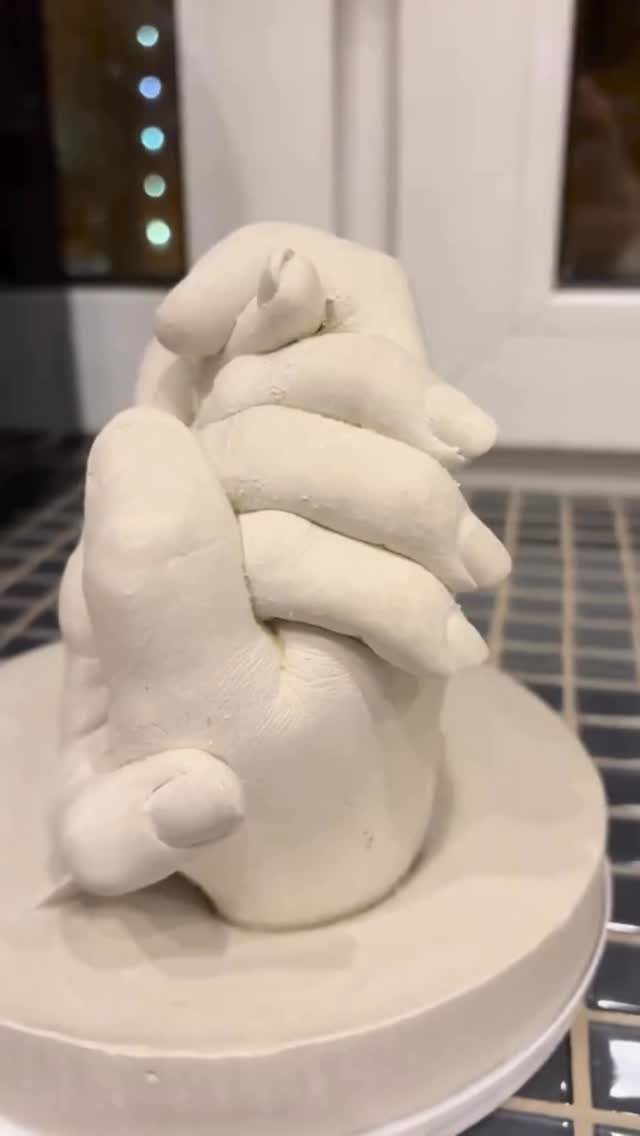 White plaster cast of two intertwined hands on a circular white base.