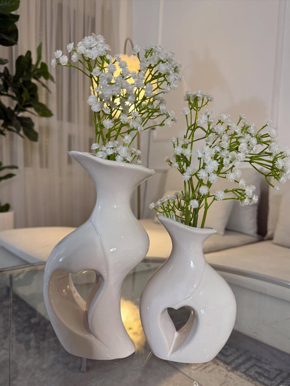 Two white ceramic vases with heart cutouts holding white baby's breath flowers.