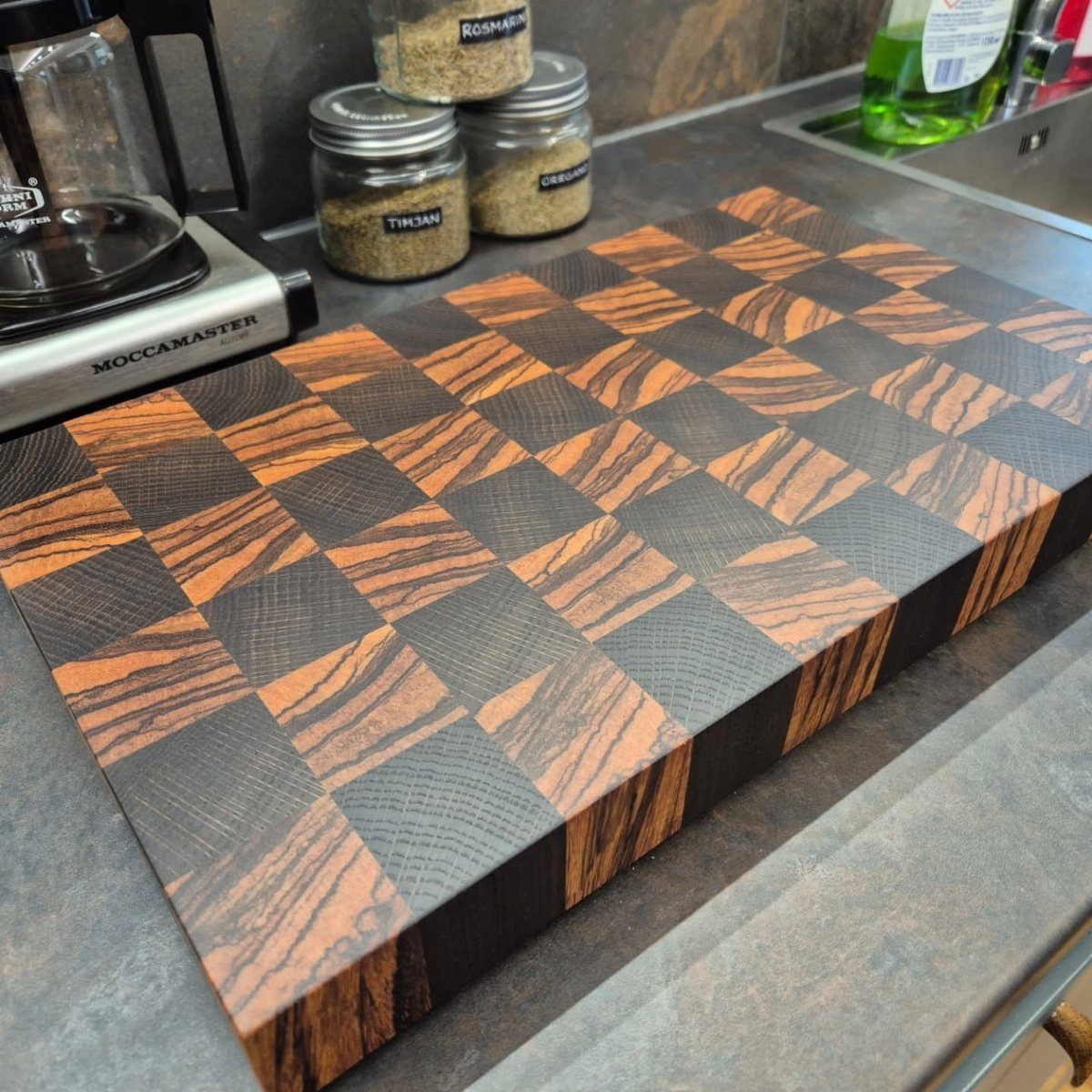 Checkered wooden cutting board on a grey kitchen counter with spice jars