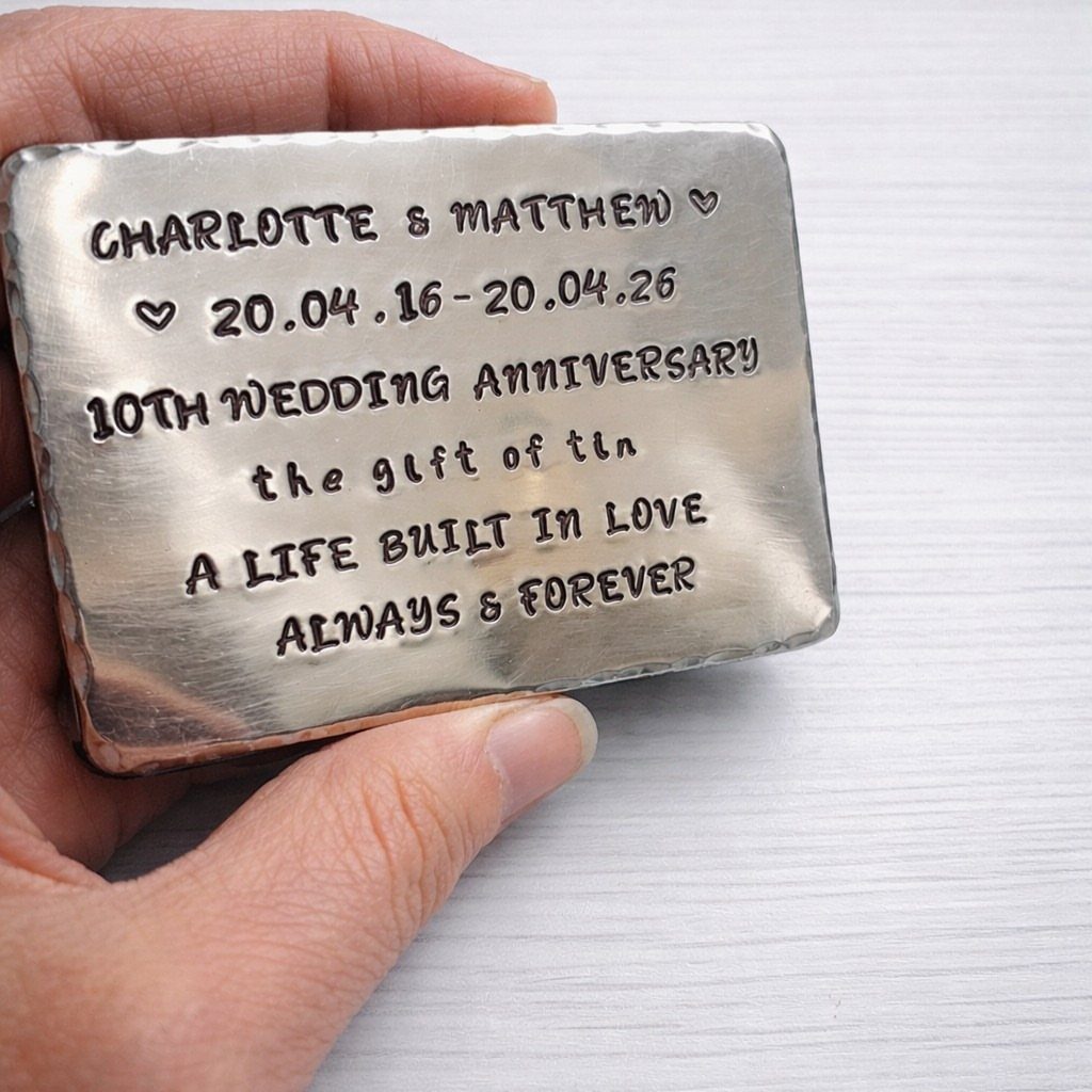 Stamped silver metal plaque commemorating a 10th wedding anniversary held in a hand.