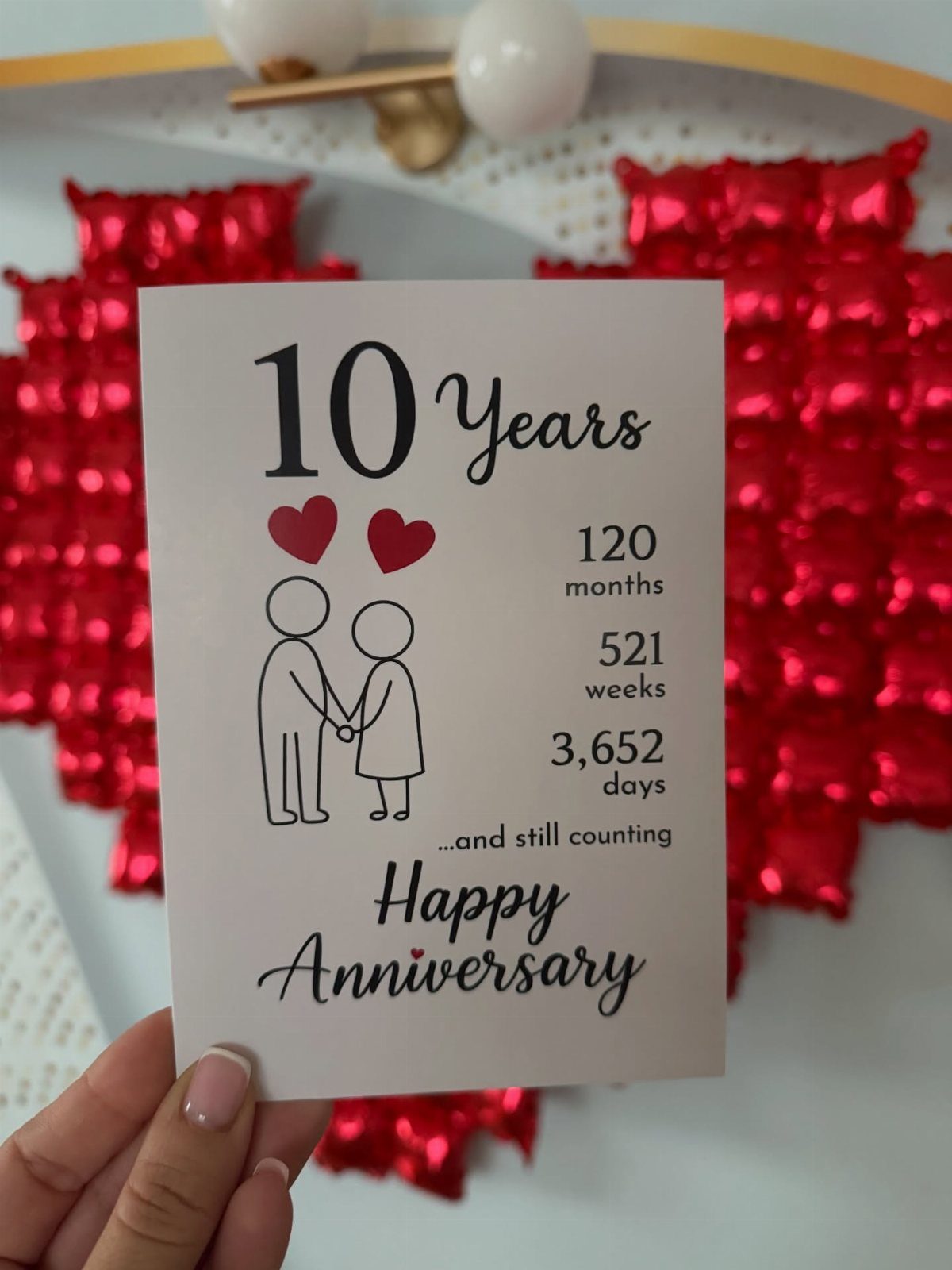 Anniversary card celebrating 10 years with a couple illustration and red heart balloons.
