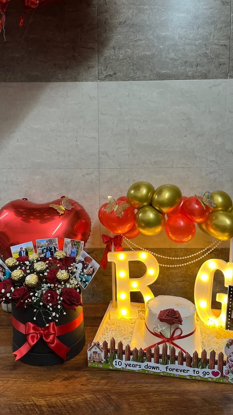Celebration setup with red roses, heart balloon, white cake, and glowing letters R and G