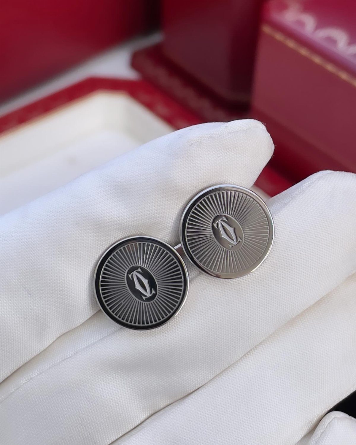 Silver circular cufflinks with radial patterns held by a white gloved hand.
