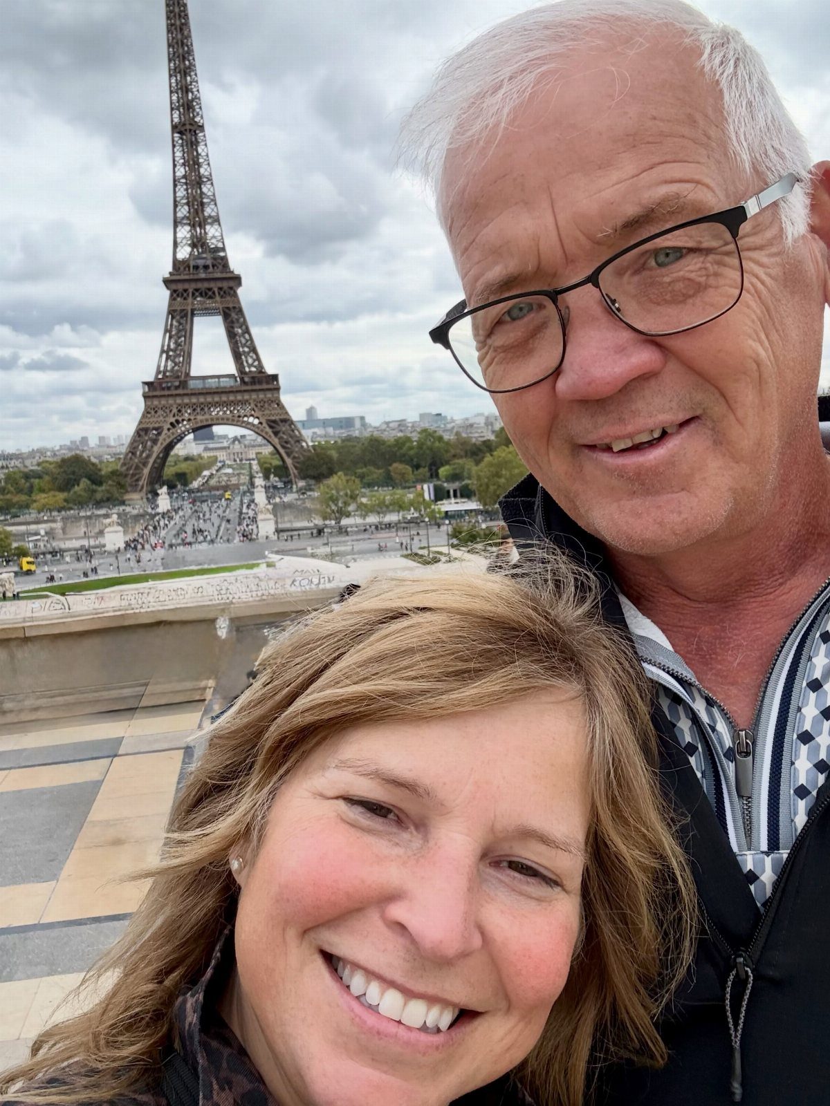 Older couple smiling for a selfie with the Eiffel Tower in Paris background.