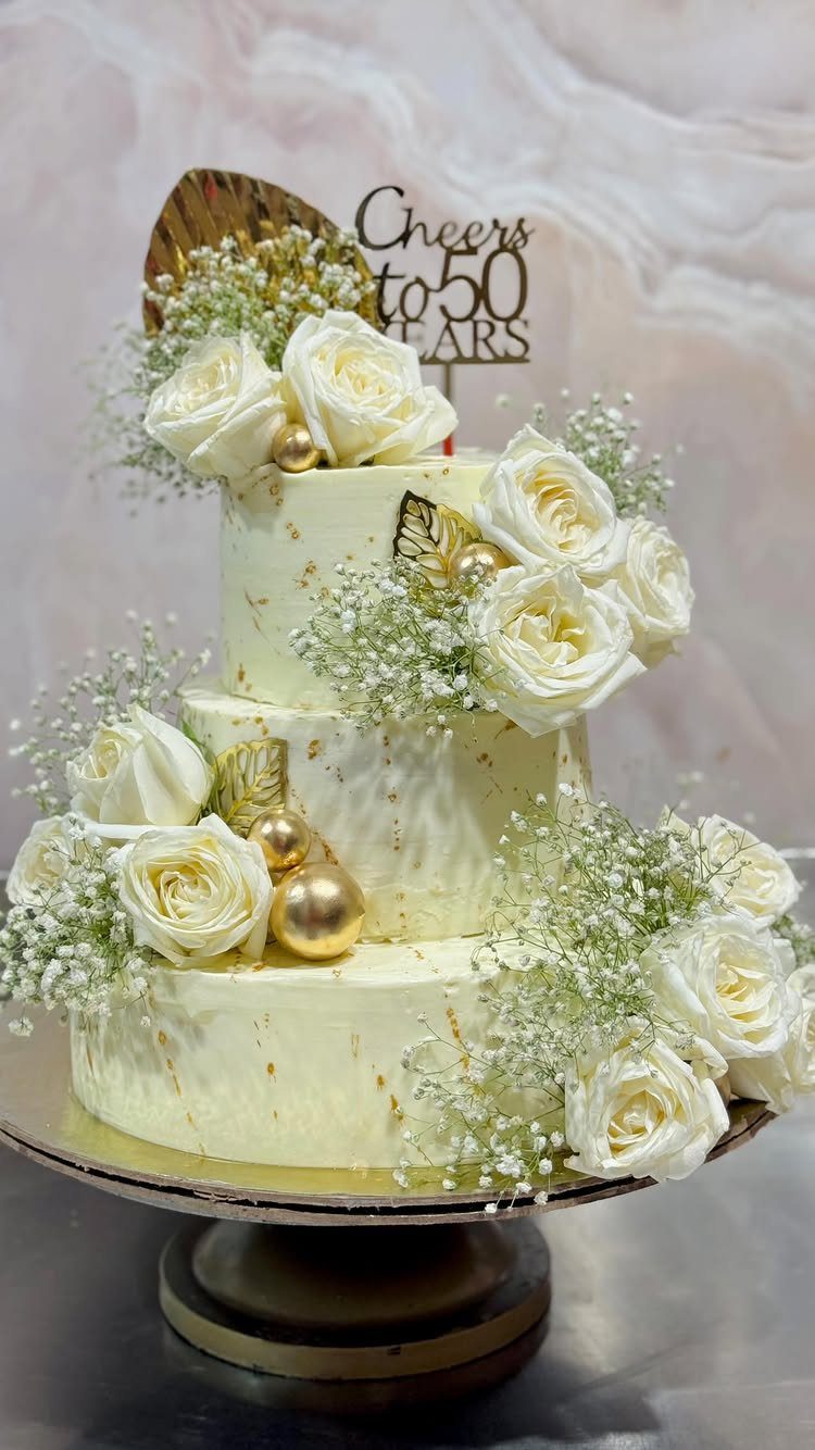 Three-tiered white anniversary cake with white roses and a gold 50 years topper.