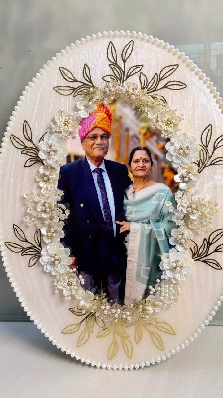 Decorative oval frame with white flowers surrounding a photo of an elderly couple.