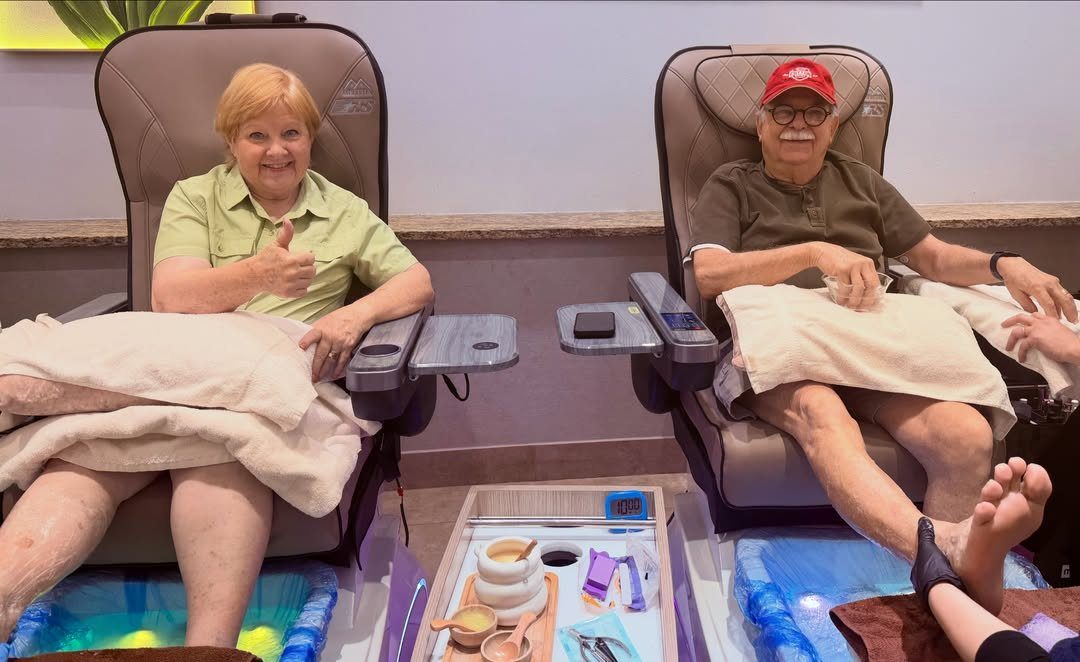 Elderly couple relaxing in pedicure chairs with glowing blue foot baths at a spa.
