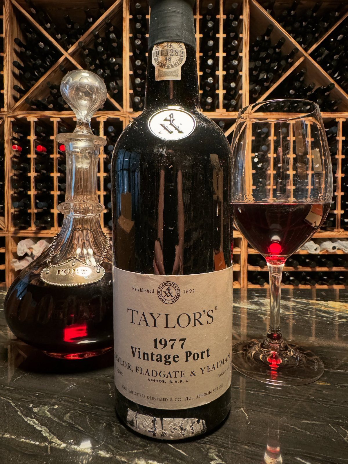 Bottle of 1977 Taylor's Vintage Port with a glass and decanter in a cellar.