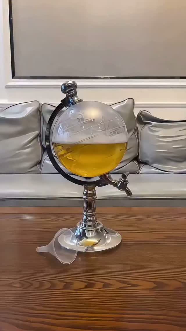 Globe-shaped glass decanter with golden liquid on a silver stand and wooden table.