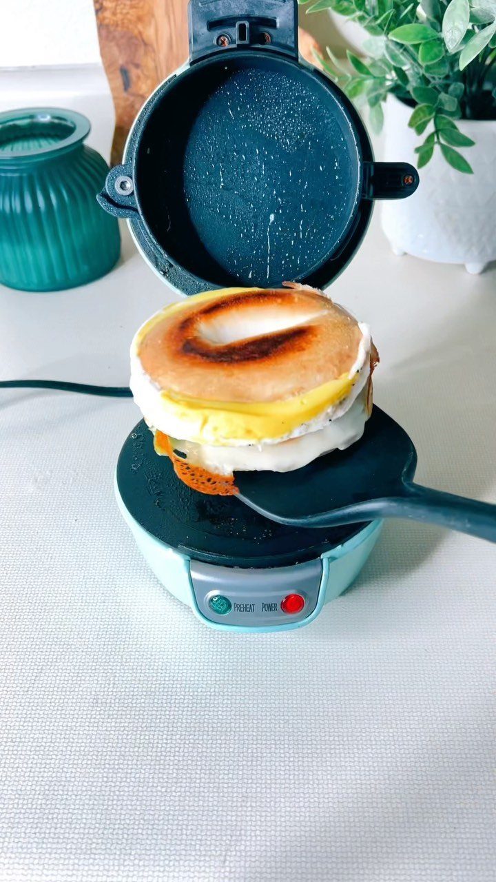 Breakfast sandwich maker with a toasted egg and cheese sandwich being lifted by spatula.