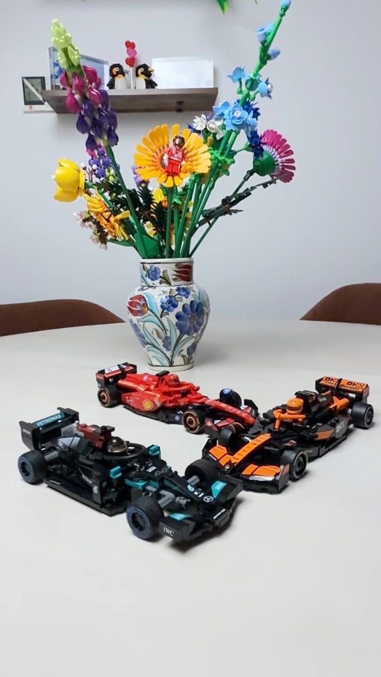 Three LEGO Formula 1 racing cars on a table with LEGO flowers in a vase