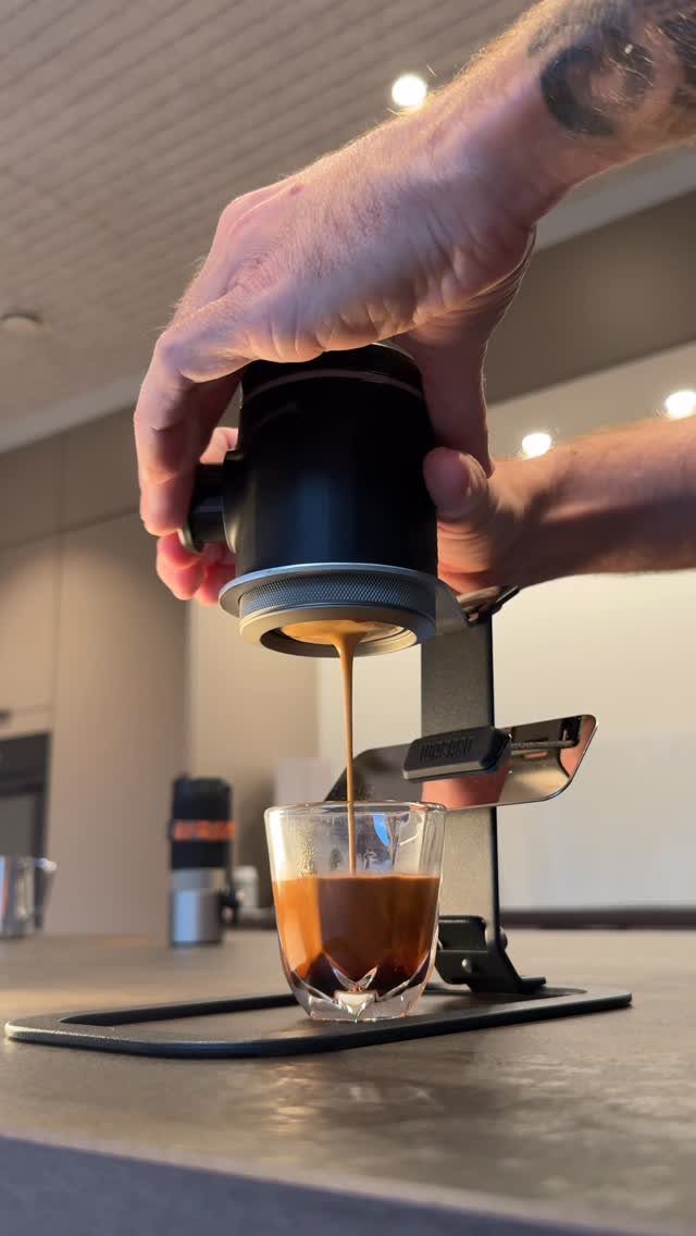 Manual espresso maker brewing coffee into a small glass on a kitchen counter