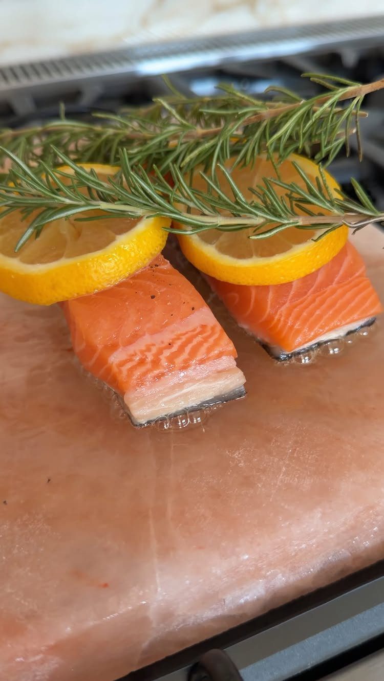 Salmon fillets with lemon and rosemary searing on a pink Himalayan salt block.