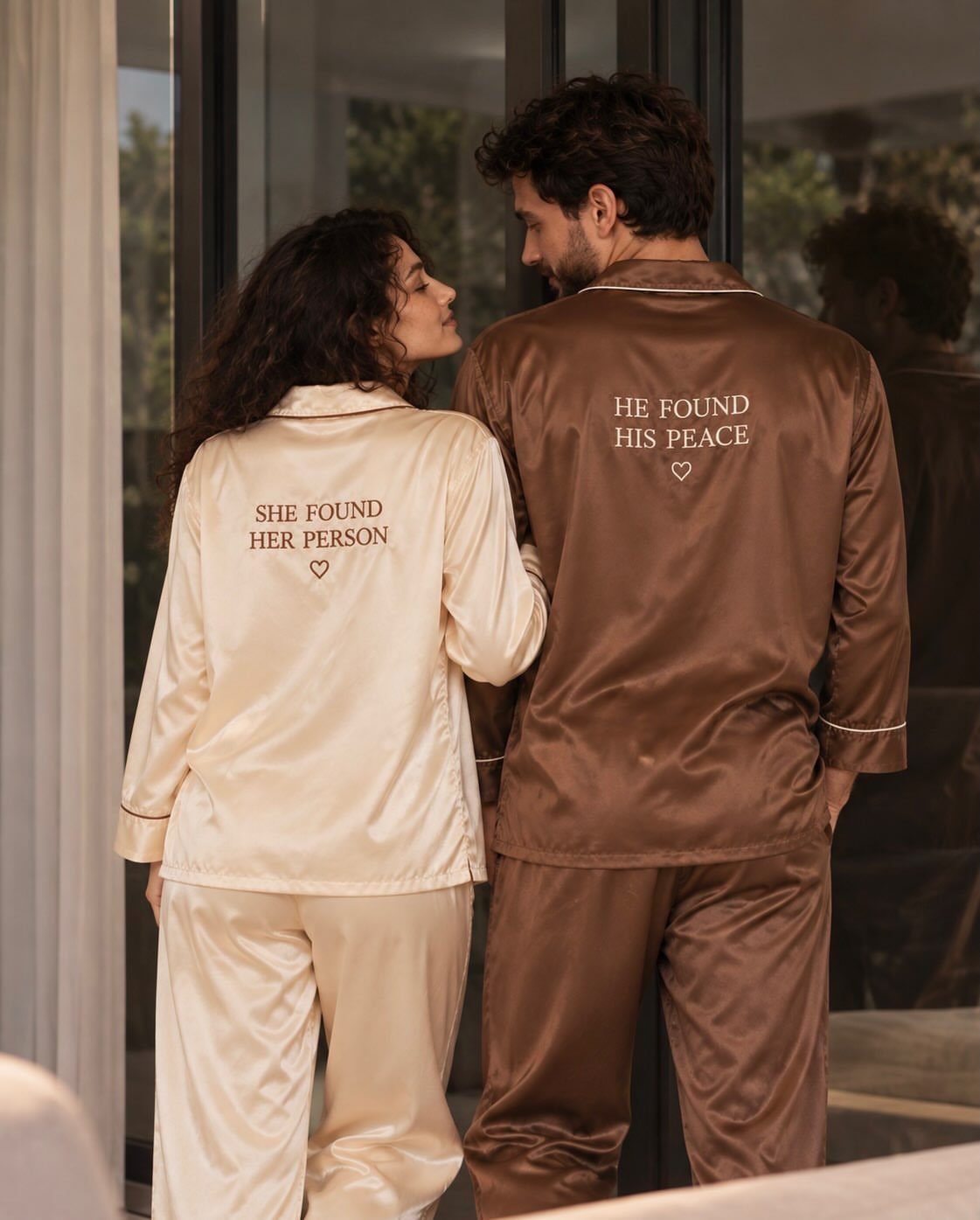 Couple wearing matching cream and brown silk pajamas with embroidered romantic quotes.