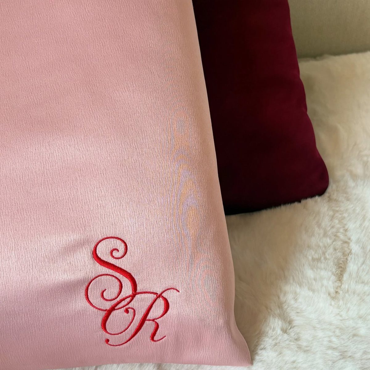 Pink and burgundy silk throw pillows on a white fluffy faux-fur rug.