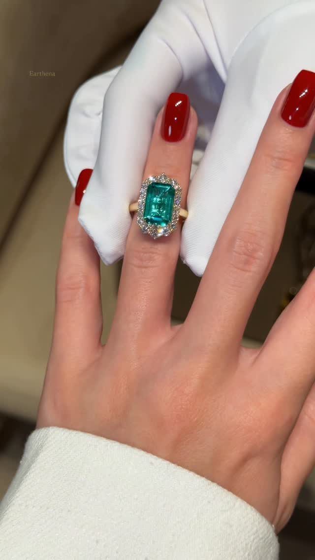 Gold ring with a large rectangular emerald and diamond halo on a finger