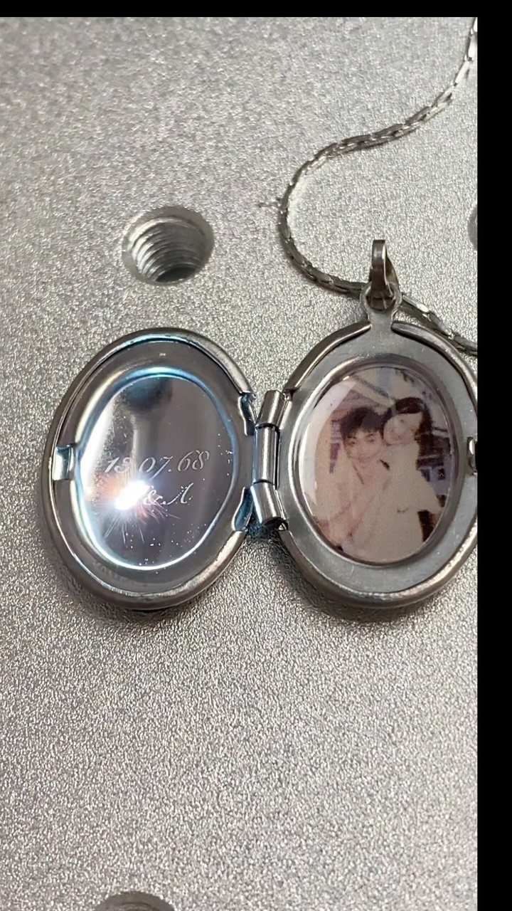 Silver heart locket open to show a couple's photo and engraved date.
