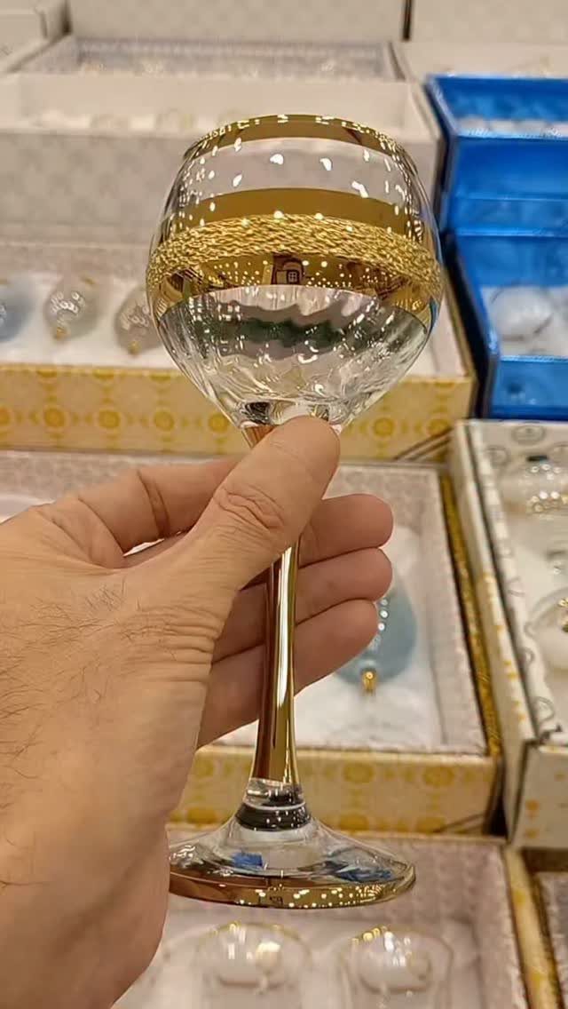 Gold-rimmed wine glass held by a hand over open gift boxes