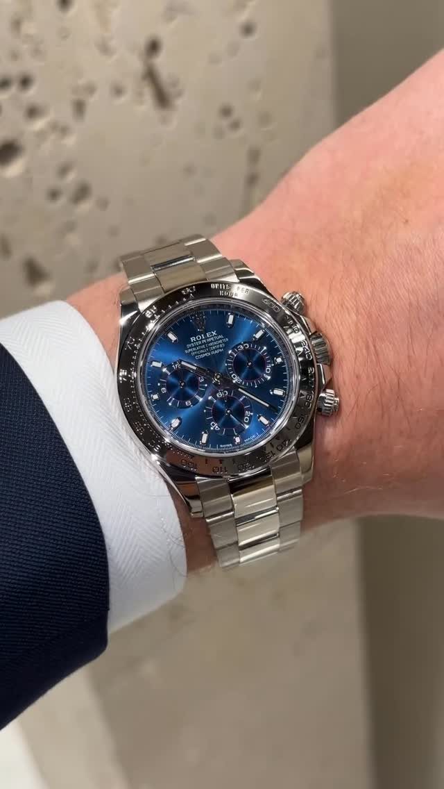 Silver luxury chronograph watch with blue dial on a wrist wearing a suit.