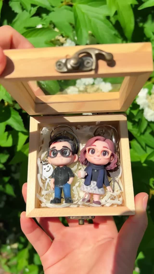 Custom clay couple figurines in a small wooden display box held outdoors.