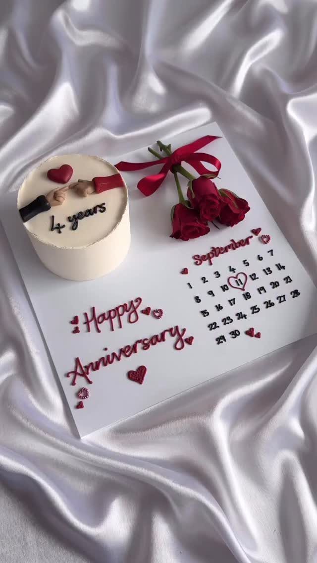 Small white anniversary cake and red roses on a calendar board with satin fabric.