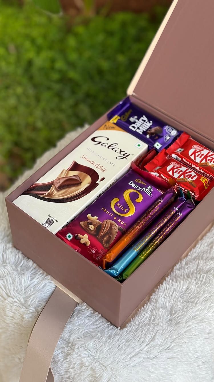 Mauve gift box filled with assorted chocolate bars on a white fluffy rug.