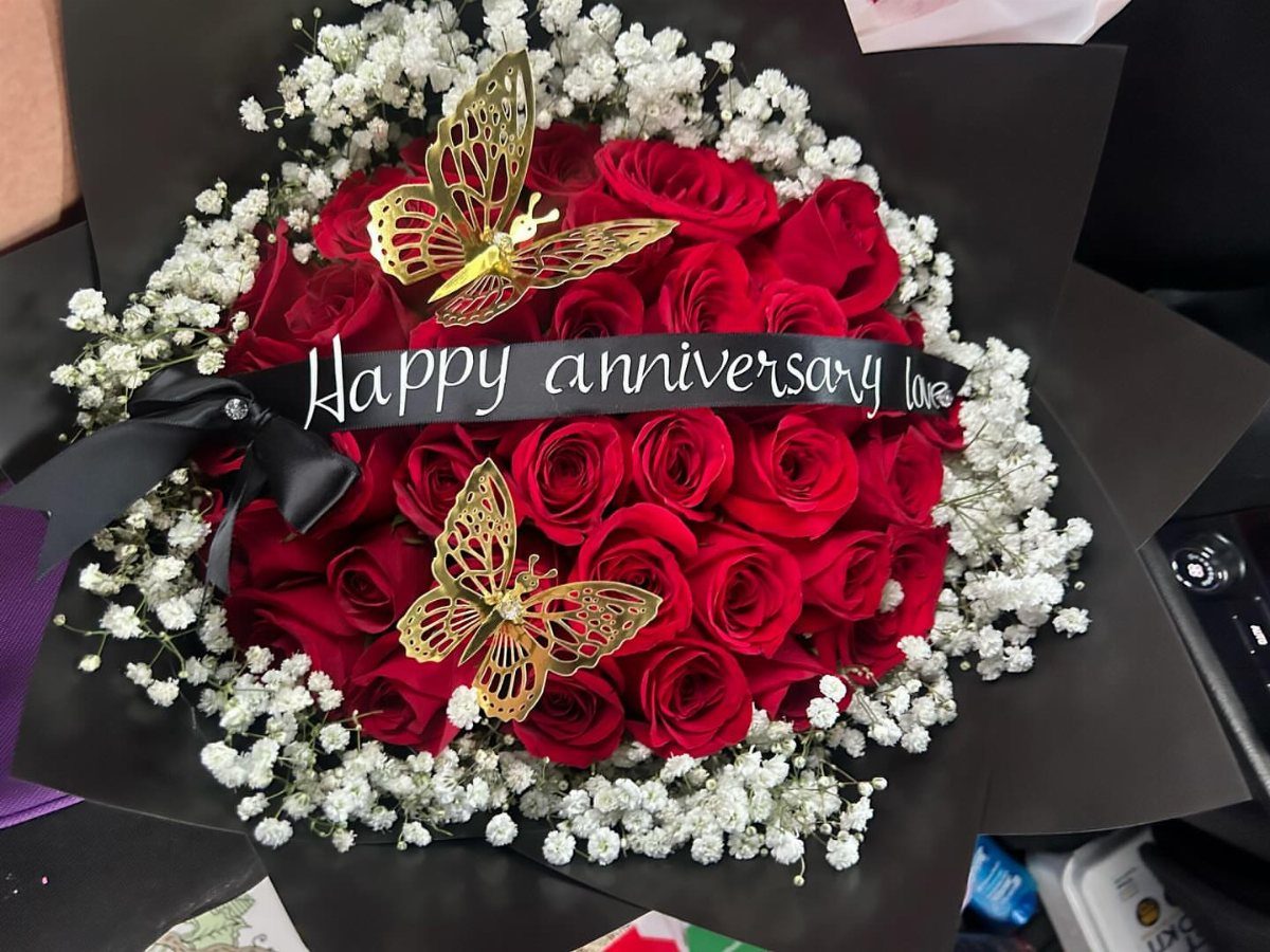 Red rose bouquet with white baby's breath, gold butterflies, and anniversary ribbon.