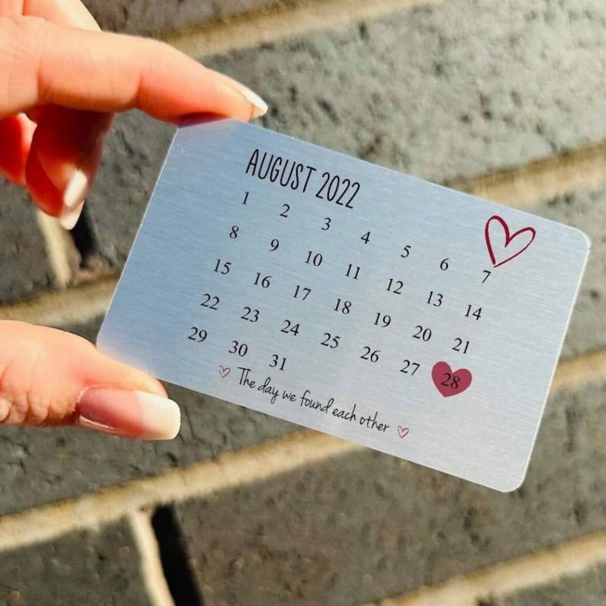 Engraved silver metal calendar card with red hearts held by a hand.