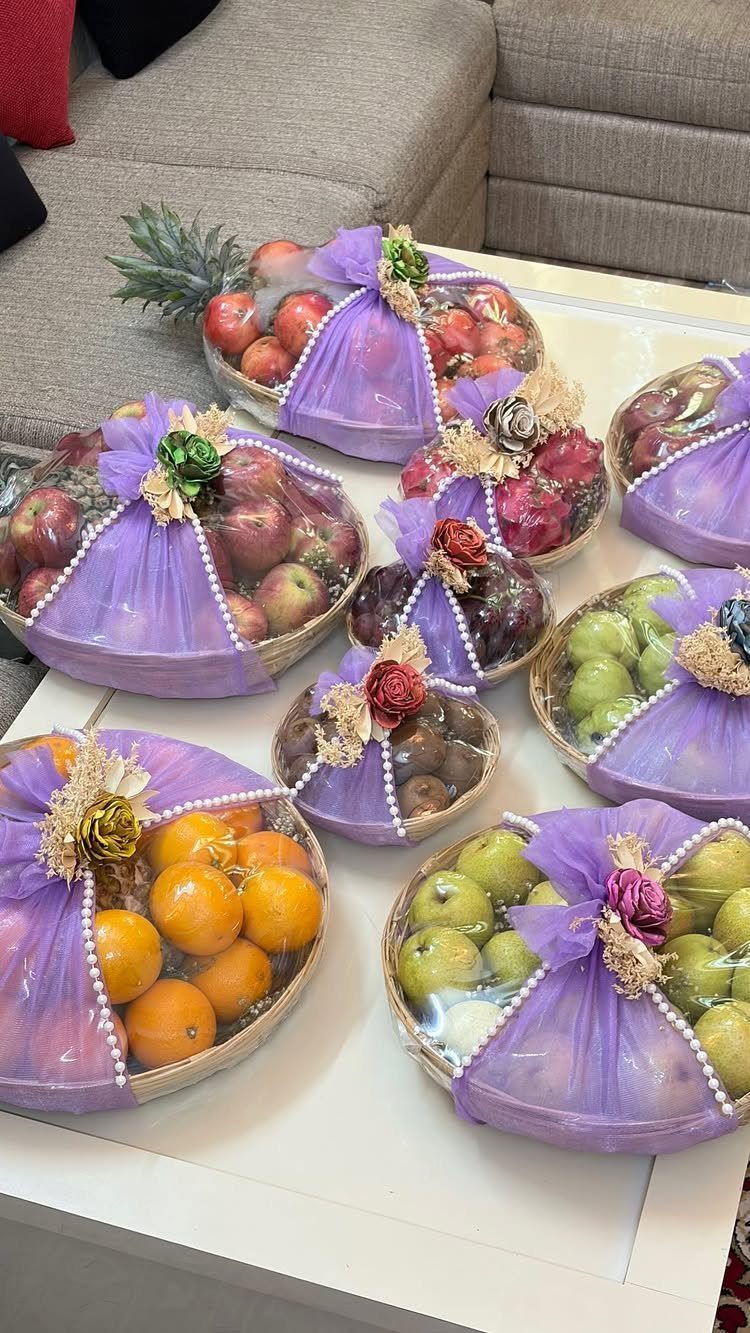 Fresh fruit gift baskets wrapped in purple tulle with decorative bows on white table