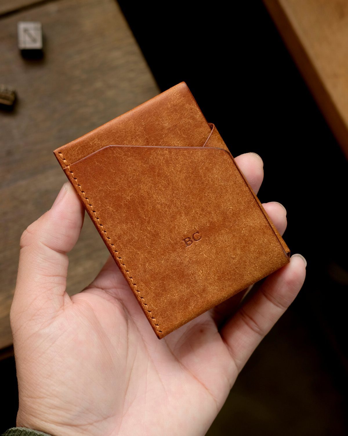 Tan leather wallet with engraved initials BC held in a person's hand.