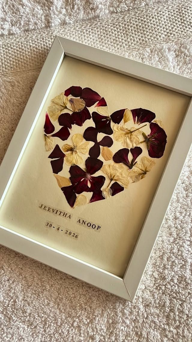 Pressed flower petals arranged in a heart shape inside a white picture frame.