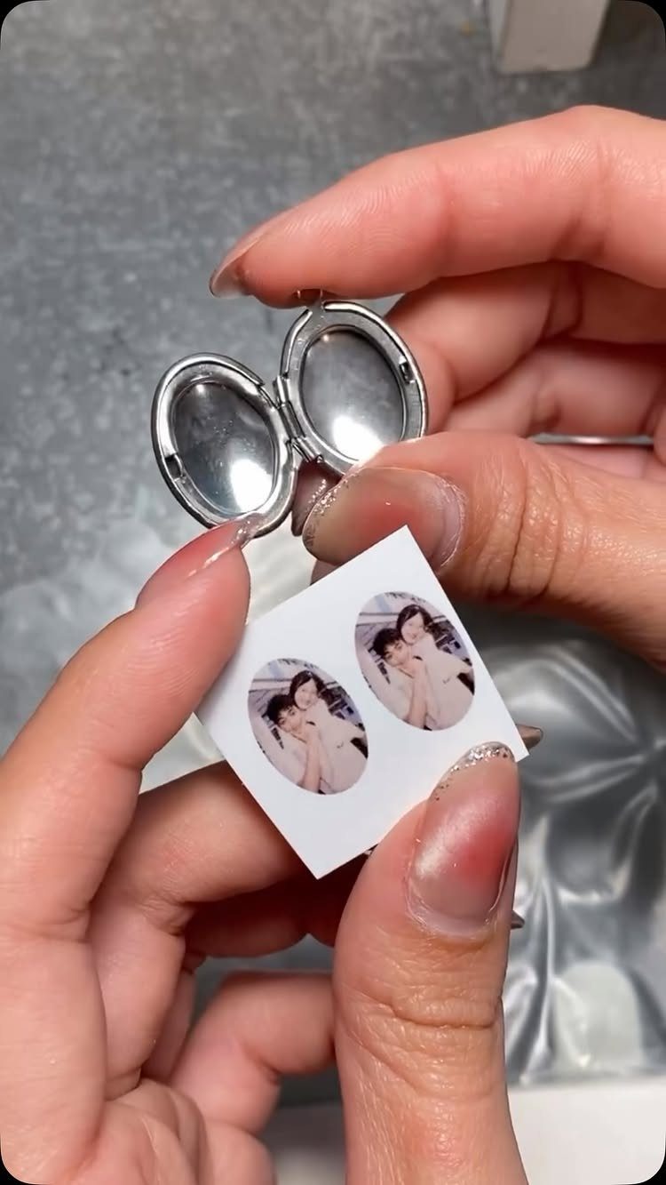 Silver oval locket and small couple photos being prepared for insertion.