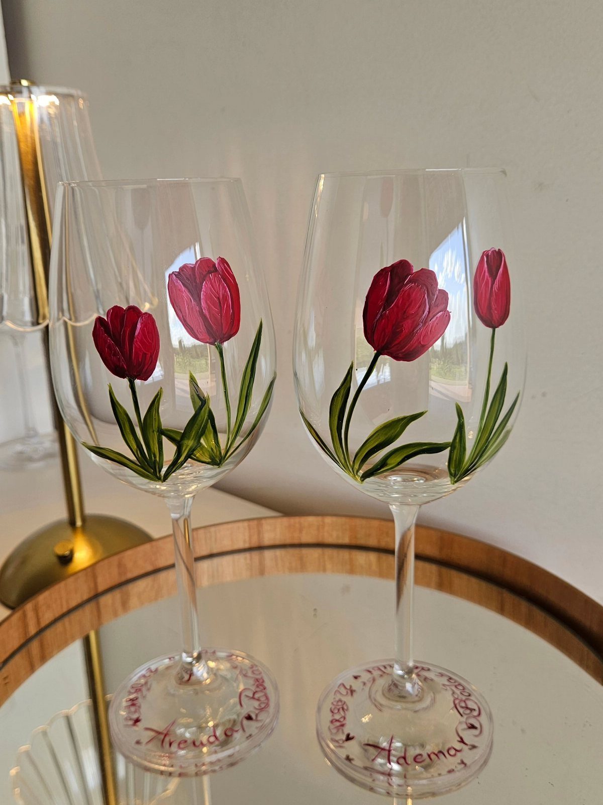 Two wine glasses with hand-painted red tulips and red text on the bases.