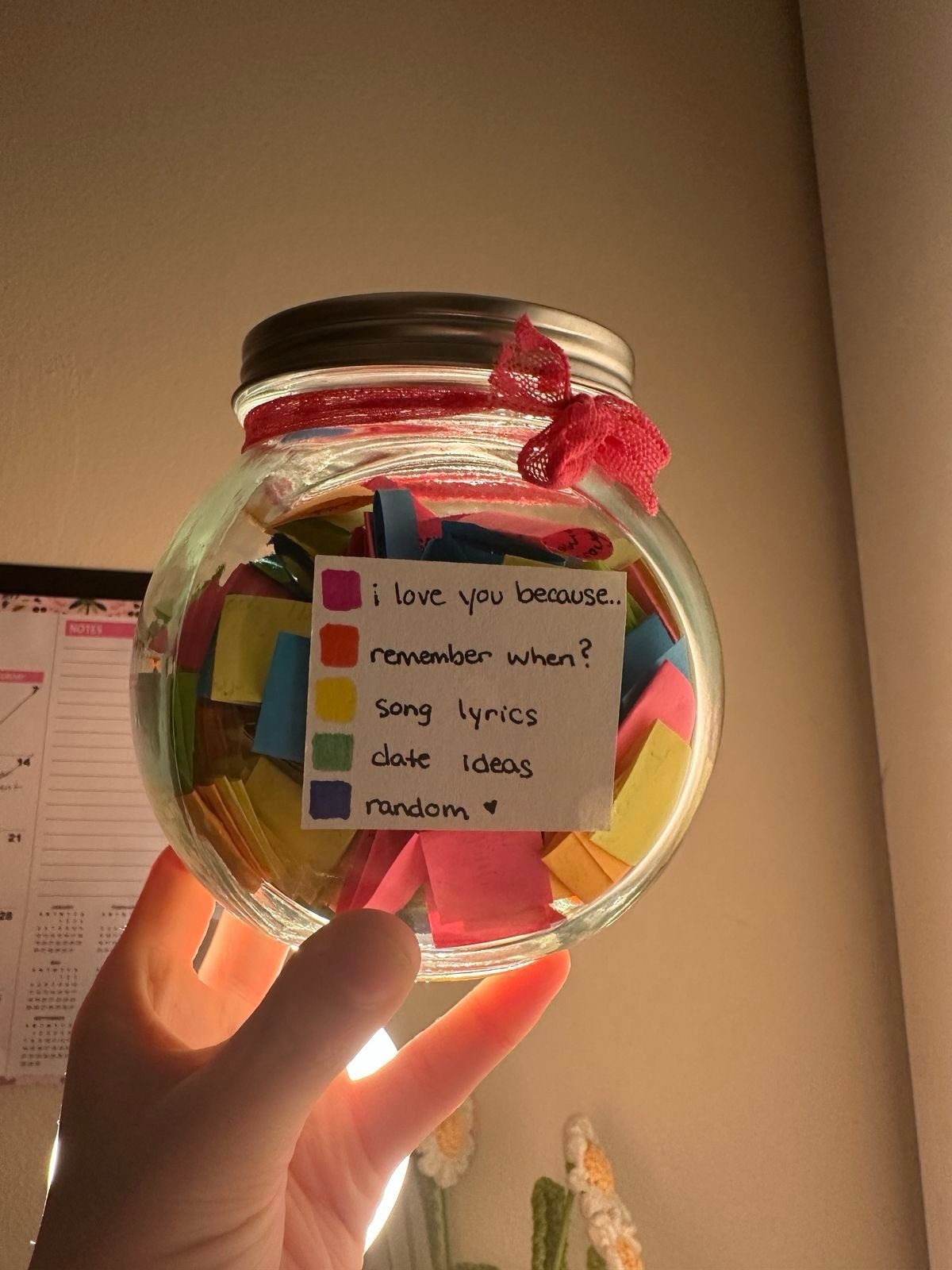 Glass mason jar filled with colorful memory slips and a red ribbon tie.