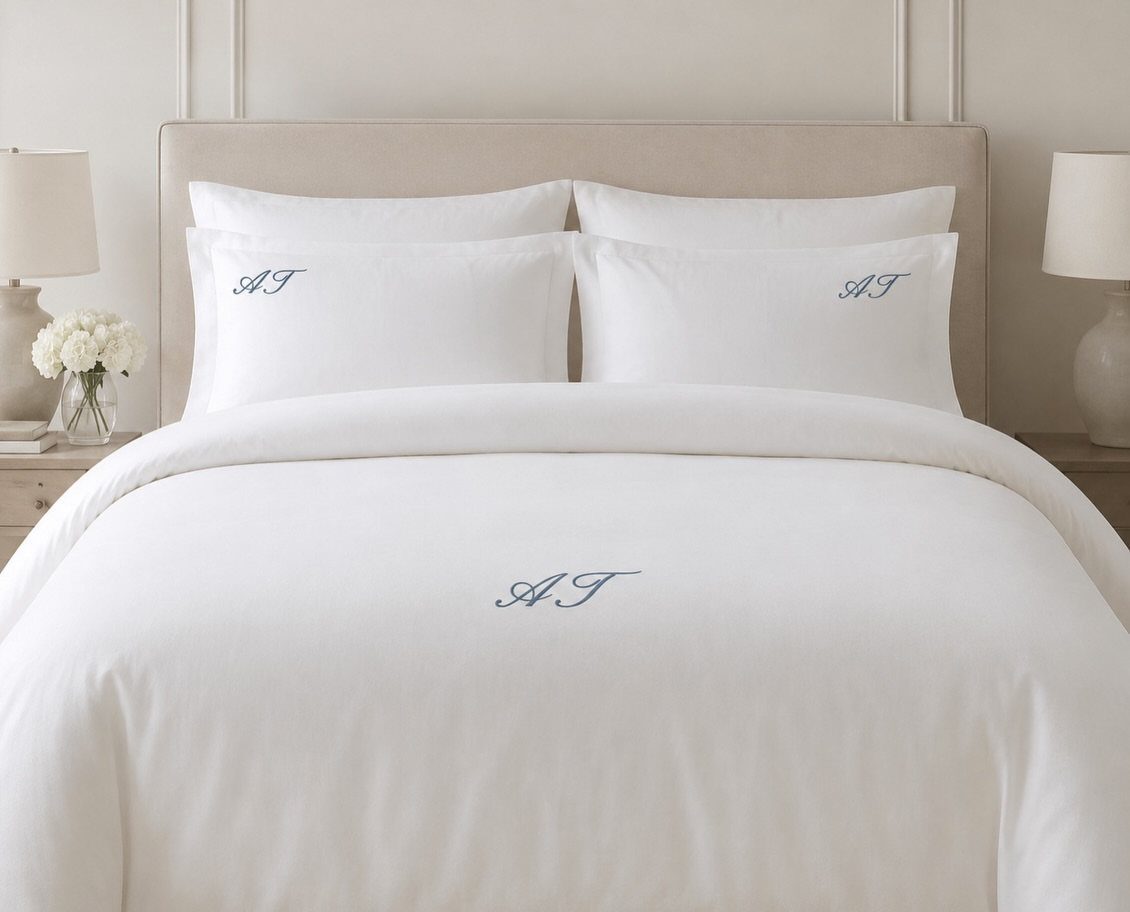 White bedding with embroidered blue initials on pillows and a duvet cover.