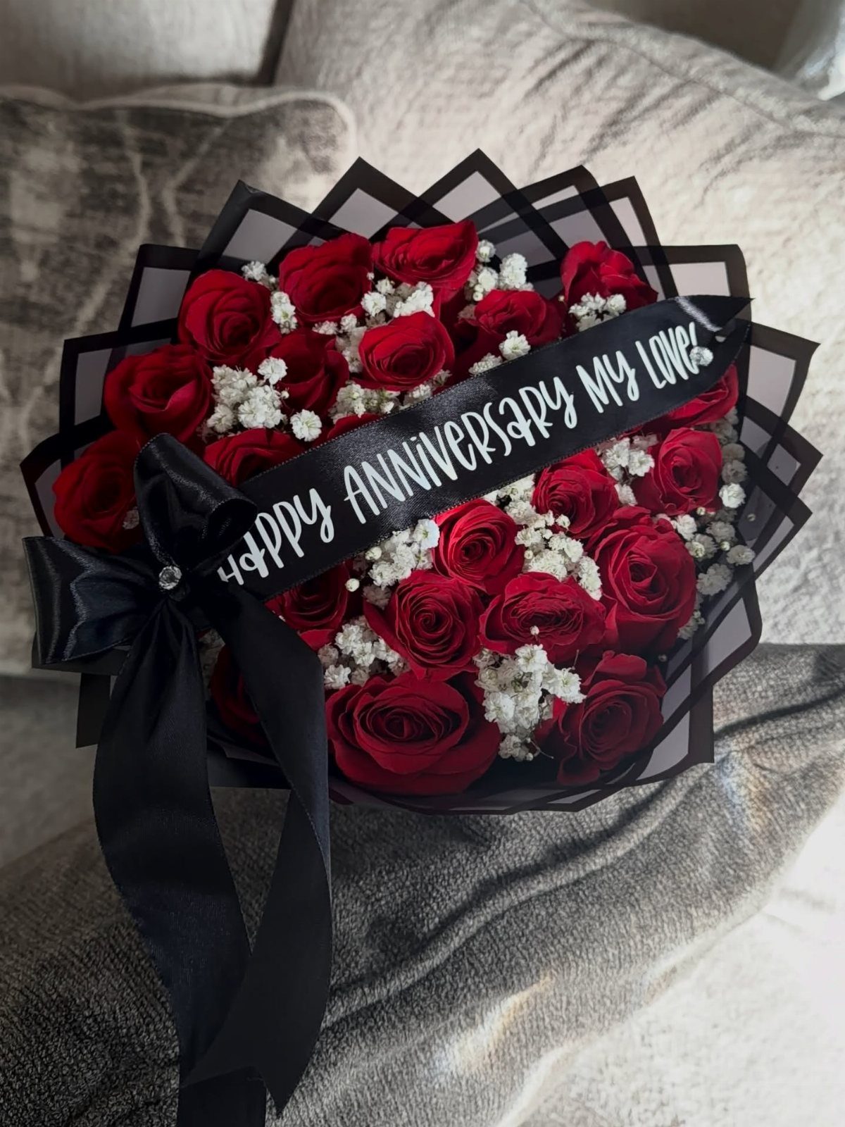Bouquet of red roses and baby's breath with anniversary ribbon on a sofa.
