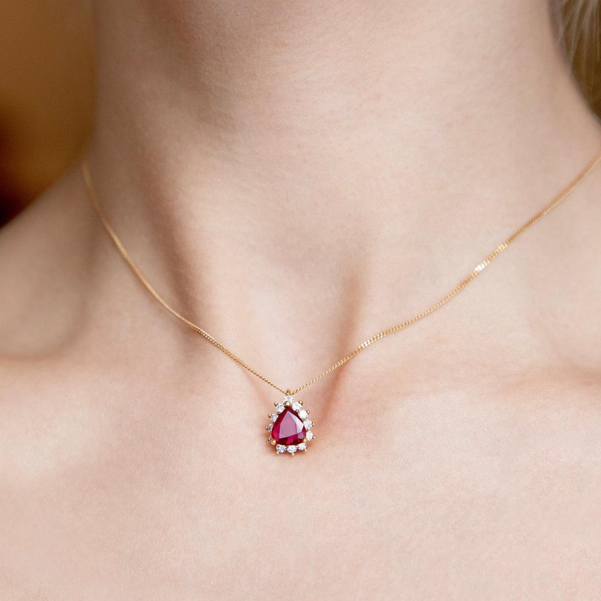 Gold necklace with a pear-shaped red ruby pendant worn on a person's neck.