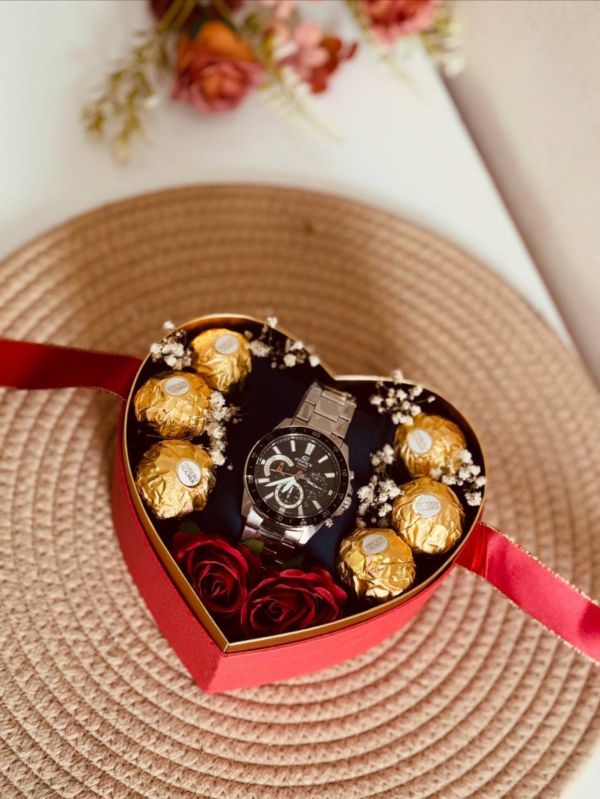 Silver wristwatch and gold chocolates in a heart-shaped red gift box with roses.