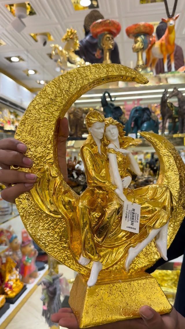 Gold figurine of a couple sitting in a crescent moon held by hands