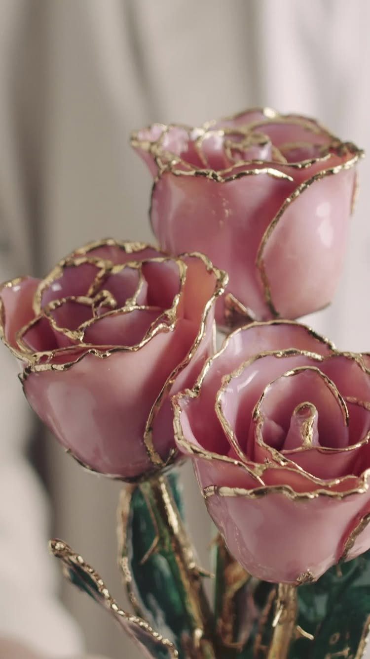 Three pink roses with gold-dipped petal edges and gold stems with green leaves.