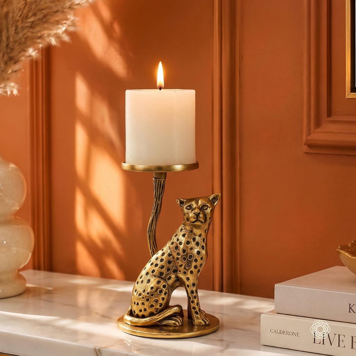Gold leopard candle holder with a lit white pillar candle on marble surface