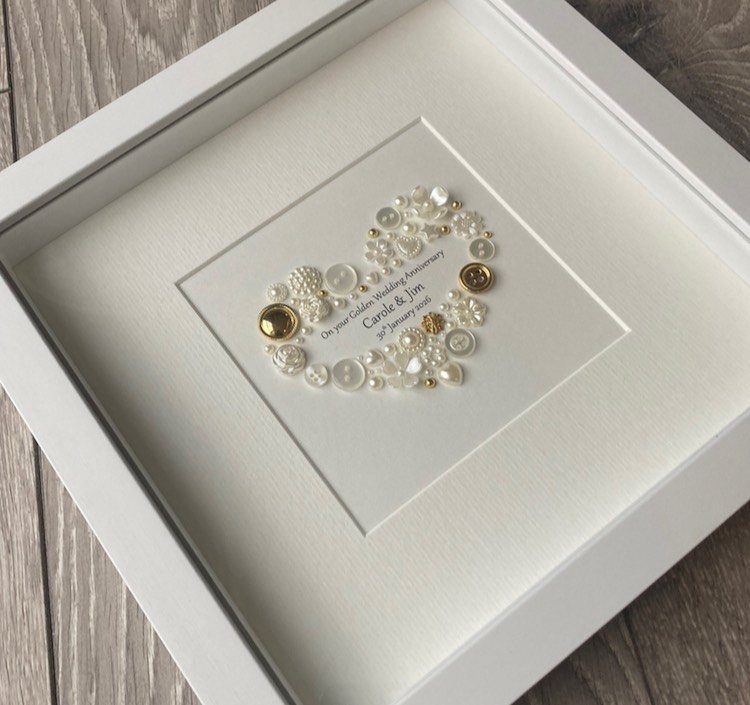 Heart made of white and gold buttons in a white frame for anniversary.