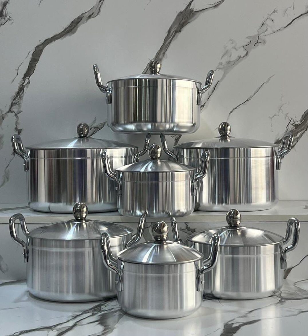 Silver aluminum pots of various sizes arranged on a white marble surface.