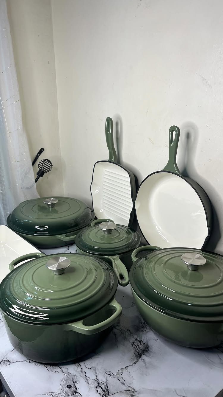 Green enameled cast iron pots and pans on a white marble surface.
