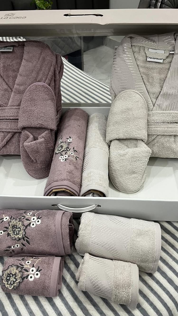 Luxury spa gift set with mauve and grey robes, slippers, and embroidered towels.