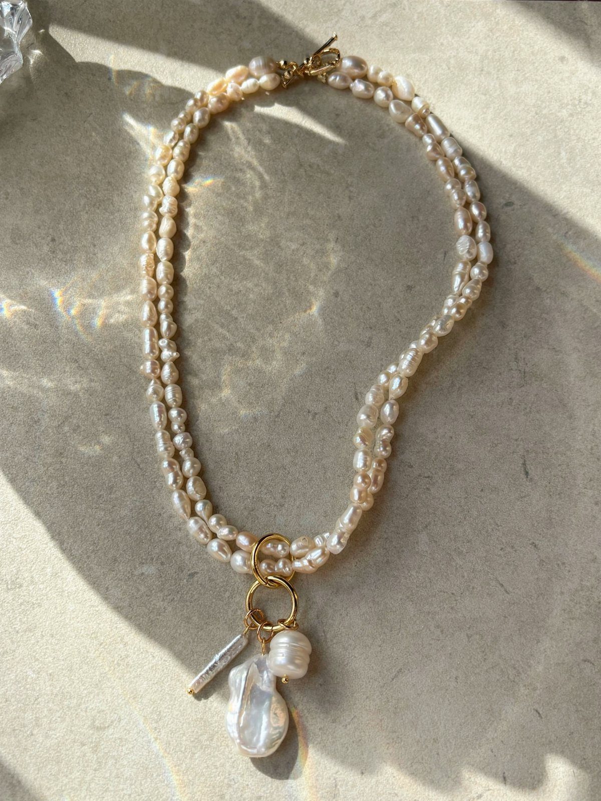 Double-strand cream pearl necklace with a baroque pearl charm on a beige surface