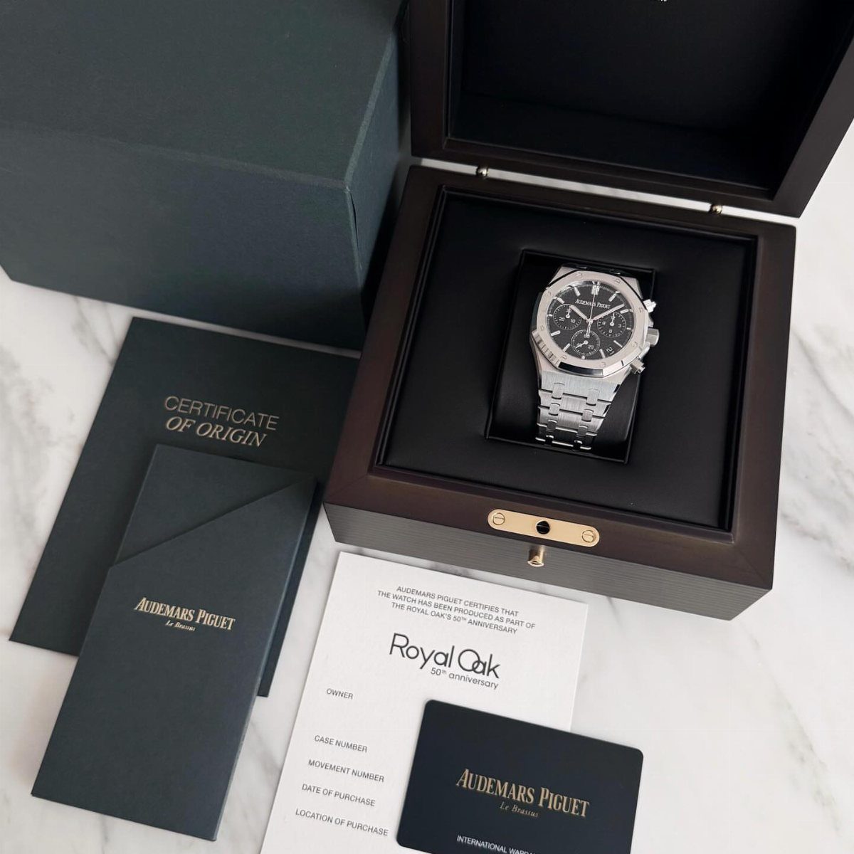Silver luxury wristwatch in a wooden box with official brand certificates on marble.